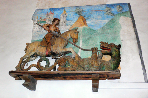  ... ein heiliger Georg streckte den Drachen nieder auf dem Giebel einer Fassade, die, wie auch er, mit kleinen Holzschuppen bedeckt war. [Original in der Kirche 